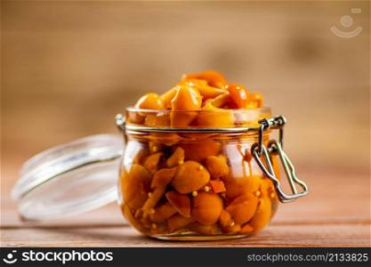 Glass jar with marinated mushrooms. On a wooden background. High quality photo. Glass jar with marinated mushrooms.