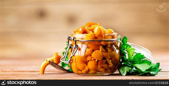Glass jar with marinated mushrooms. On a wooden background. High quality photo. Glass jar with marinated mushrooms.