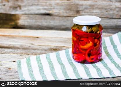 Glass jar with pickled red bell peppers.Preserved food concept, canned vegetables isolated in a rustic composition.