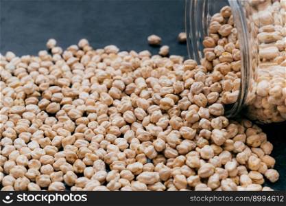 Glass jar with raw garbanzo. Chickpea grains isolated on dark background. Close up shot. Protein seeds. Healthy food. Vegan ingredient