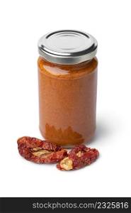 Glass jar with red Italian pesto and dried sweet tomatoes in front isolated on white background