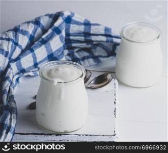 glass jars with homemade yogurt on a white wooden board, close up