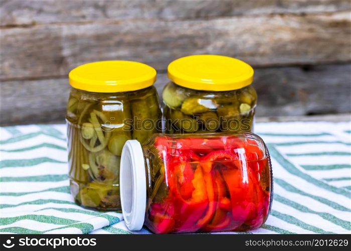 Glass jars with pickled red bell peppers and pickled cucumbers (pickles) isolated. Jars with variety of pickled vegetables. Preserved food concept in a rustic composition.. Glass jars with pickled red bell peppers and pickled cucumbers (pickles) isolated. Jars with variety of pickled vegetables. Preserved food concept in a rustic composition.