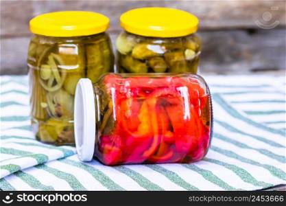 Glass jars with pickled red bell peppers and pickled cucumbers (pickles) isolated. Jars with variety of pickled vegetables. Preserved food concept in a rustic composition.. Glass jars with pickled red bell peppers and pickled cucumbers (pickles) isolated. Jars with variety of pickled vegetables. Preserved food concept in a rustic composition.