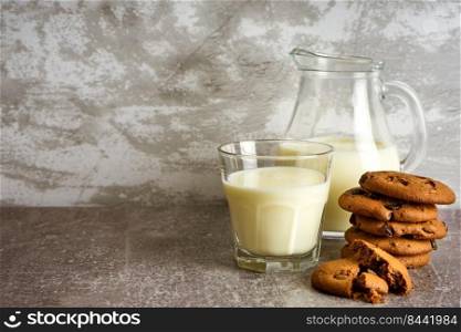 Glass jug and glass with milk and chocolate cookie on gray background with copy space.. Glass jug and glass with milk on gray background.