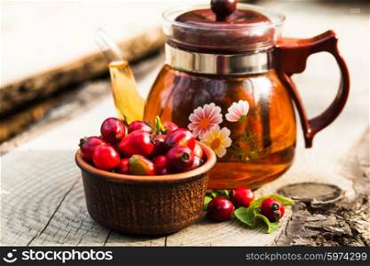 Glass kettle with tea and bowl with berry of a dogrose. Flavored dogrose tea
