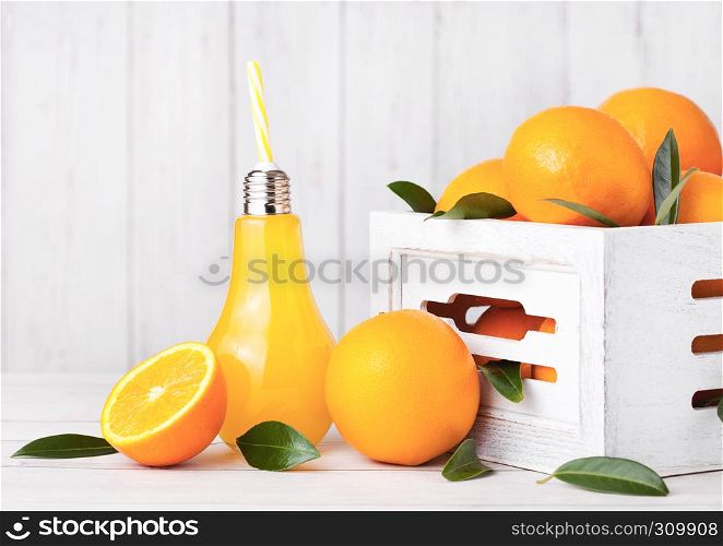 Glass lamp shape of organic fresh orange juice with raw oranges in white wooden box