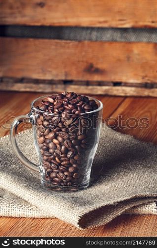 Glass mug with beans on burlap napkin on wooden background. Glass mug with beans on burlap napkin