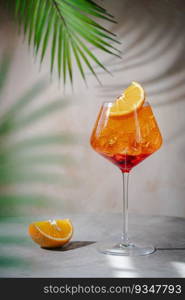 Glass of Aperol spritz cocktail with fresh oranges and palm leaves on beige background. natural light and shadows. Glass of Aperol spritz cocktail