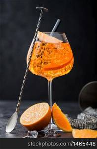 Glass of aperol spritz summer cocktail with orange slices and bar spoon with cocktail shaker on black background. Ice cubes and black straw.