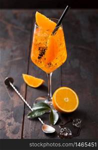 Glass of aperol spritz summer cocktail with orange slices and bar spoon on wooden background with ice cubes. Top view