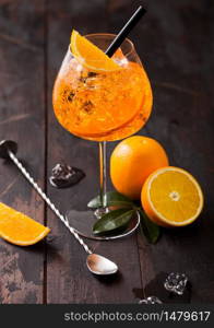 Glass of aperol spritz summer cocktail with orange slices and bar spoon on wooden background with ice cubes. Top view