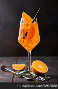 Glass of aperol spritz summer cocktail with orange slices and bar spoon on wooden background with ice cubes.