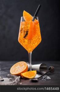 Glass of aperol spritz summer cocktail with orange slices and strainer with jigger on black background with ice cubes.