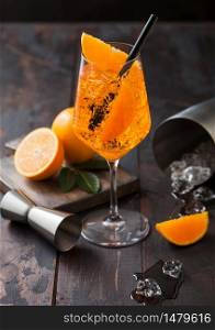 Glass of aperol spritz summer cocktail with oranges and bar spoon with cocktail shaker on wooden background with ice cubes.
