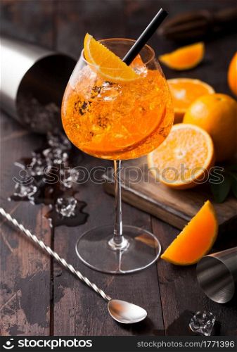 Glass of aperol spritz summer cocktail with oranges and cocktail shaker with bar spoon on wooden background with ice cubes. Top view
