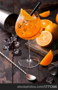 Glass of aperol spritz summer cocktail with oranges and cocktail shaker with bar spoon on wooden background with ice cubes. Top view