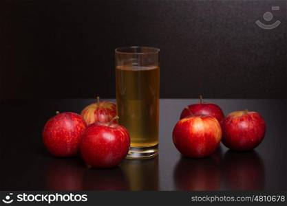 Glass of apple juice and a red apples on a dark wooden background
