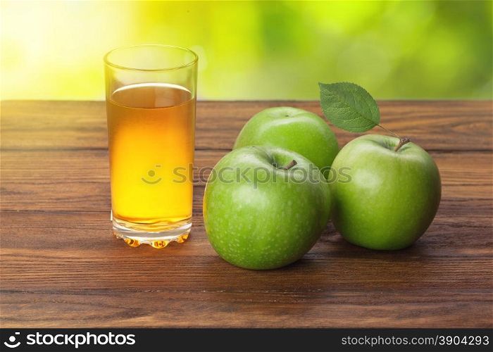 Glass of apple juice and apples on wooden background