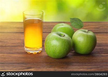 Glass of apple juice and apples on wooden background