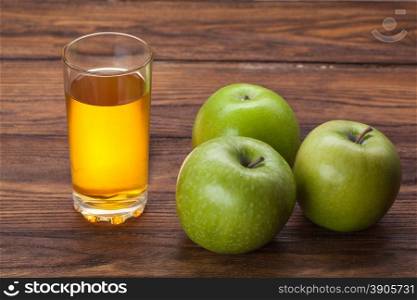 Glass of apple juice and green apples on wooden background