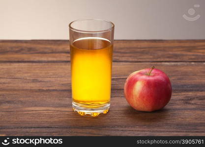 Glass of apple juice and red apple on wooden background