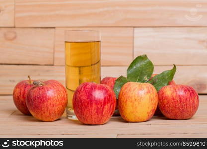 Glass of apple juice and red apples on wooden background