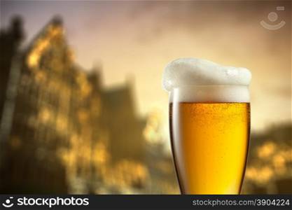 Glass of beer against blurred european city with beautiful lights on background at evening. Glass of beer against blurred european city