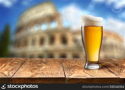 Glass of beer against Colosseum. Glass of beer on wooden table with Colosseum in Rome on background with natural bokeh
