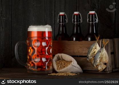 Glass of beer on table with wooden crate full of bottles, bag with beer barley and salty dried fish