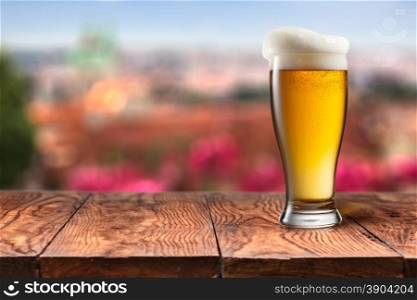 Glass of beer on wooden table against Prague. Glass of beer on wooden table with summer in Prague on background. Natural bokeh