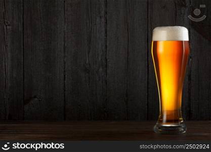 Glass of beer on wooden table, dark background with copy space