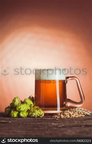 Glass of beer with hops and barley on the wooden table