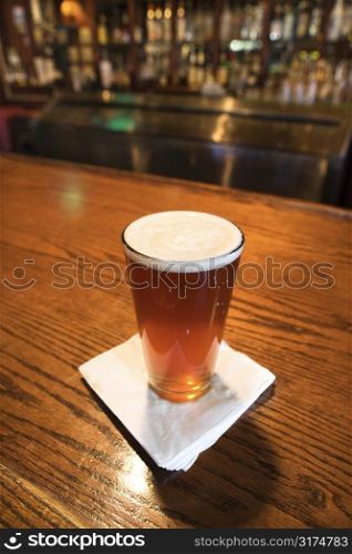 Glass of beer with napkin on bar.
