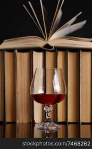 Glass of brandy on a reflective surface with books