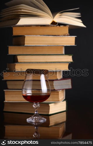 Glass of brandy on a reflective surface with books and cigar