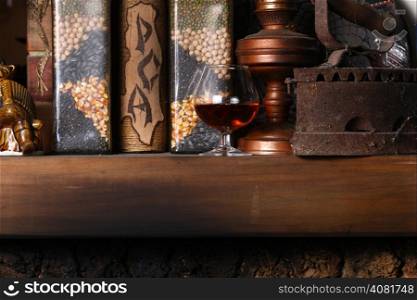 Glass of brandy standing on a fireplace shelf with various vintage objects
