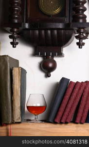 Glass of brandy standing on a shelf with books under an old clock