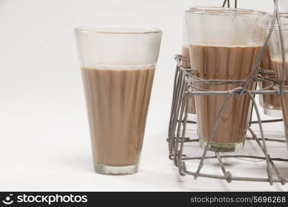 Glass of chai kept besides grid tray over white background