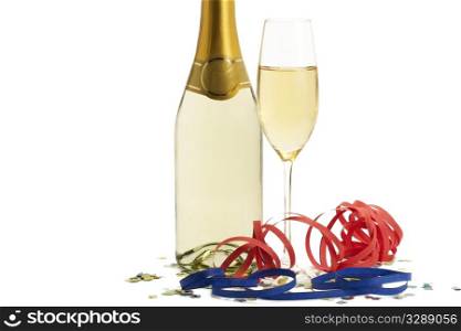 glass of champagne with blow-outs and confetti in front of a champagne bottle. glass of champagne with blow-outs and confetti in front of a champagne bottle on white background