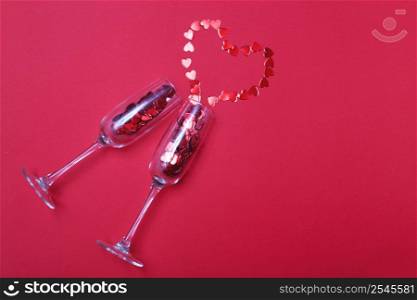 Glass of champagne with red hearts pouring in red heart shaped confetti on a red background. Valentines background, love, date concept with copy space, flat lay.. Glass of champagne with red hearts on red background. Valentines background, love, date concept with copy space
