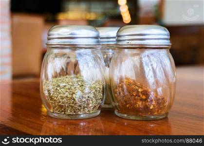 Glass of cheese salt and pepper shakers on wooden table in restaurant.