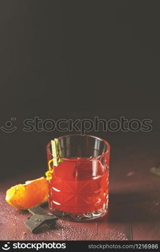 Glass of chocolate red orange negroni, an italian cocktail, an aperitif, first mixed in Firenze, Italy, in 1919, alcoholic bitter cocktail served by ingredients on the dark claret bordeaux table