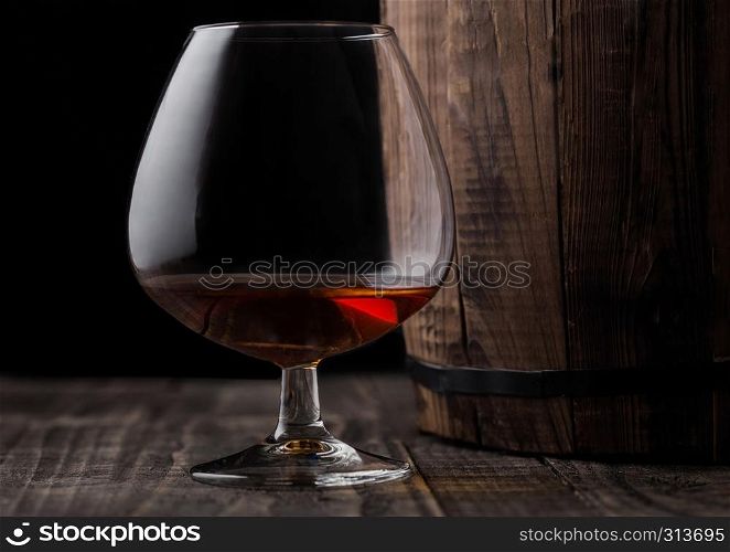 Glass of cognac brandy drink next to wooden barrel on black background.