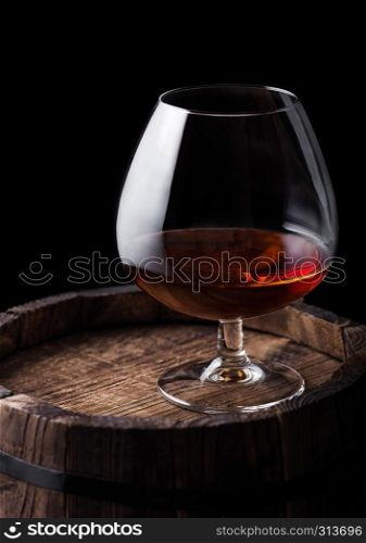 Glass of cognac brandy drink on top of wooden barrel on black background.