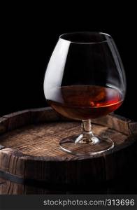Glass of cognac brandy drink on top of wooden barrel on black background.