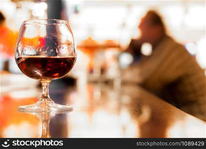 Glass of cognac on a bar stand with a silhouette of a drinking man on the background