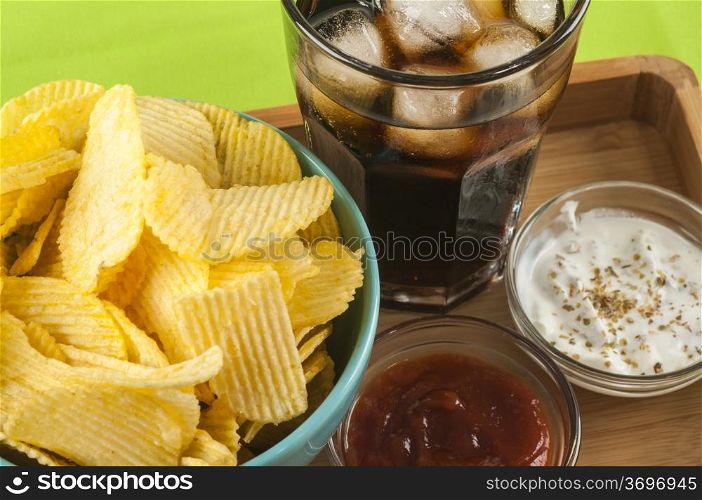 glass of coke potato crisps and ketchup and mayonnaise on bamboo tray