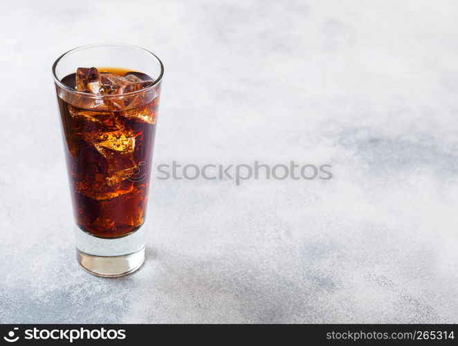 Glass of cola soda drink with ice cubes and bubbles on stone kitchen background.