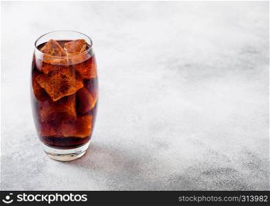Glass of cola soda drink with ice cubes and bubbles on stone kitchen background.